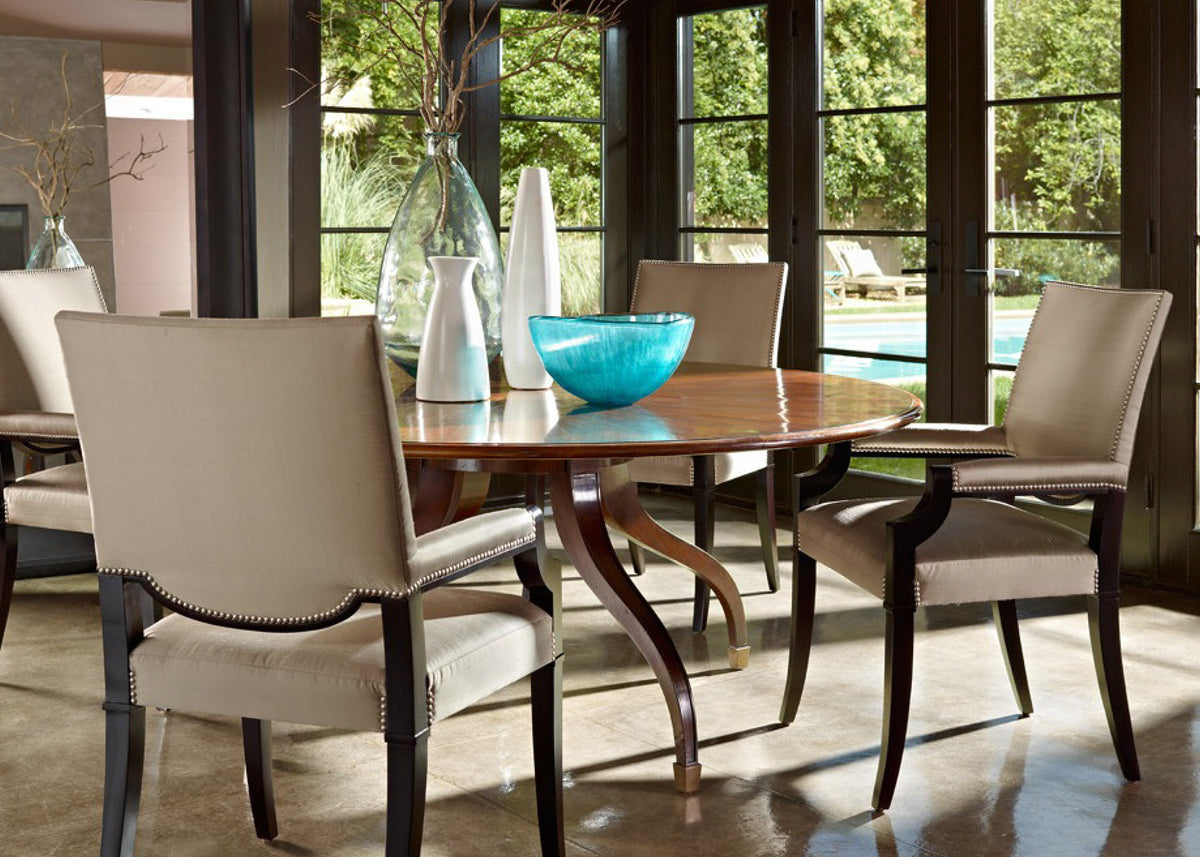 Round wood dining table with cream upholstered chairs in a sunlit room, featured by Kennedy Galleries Toronto.