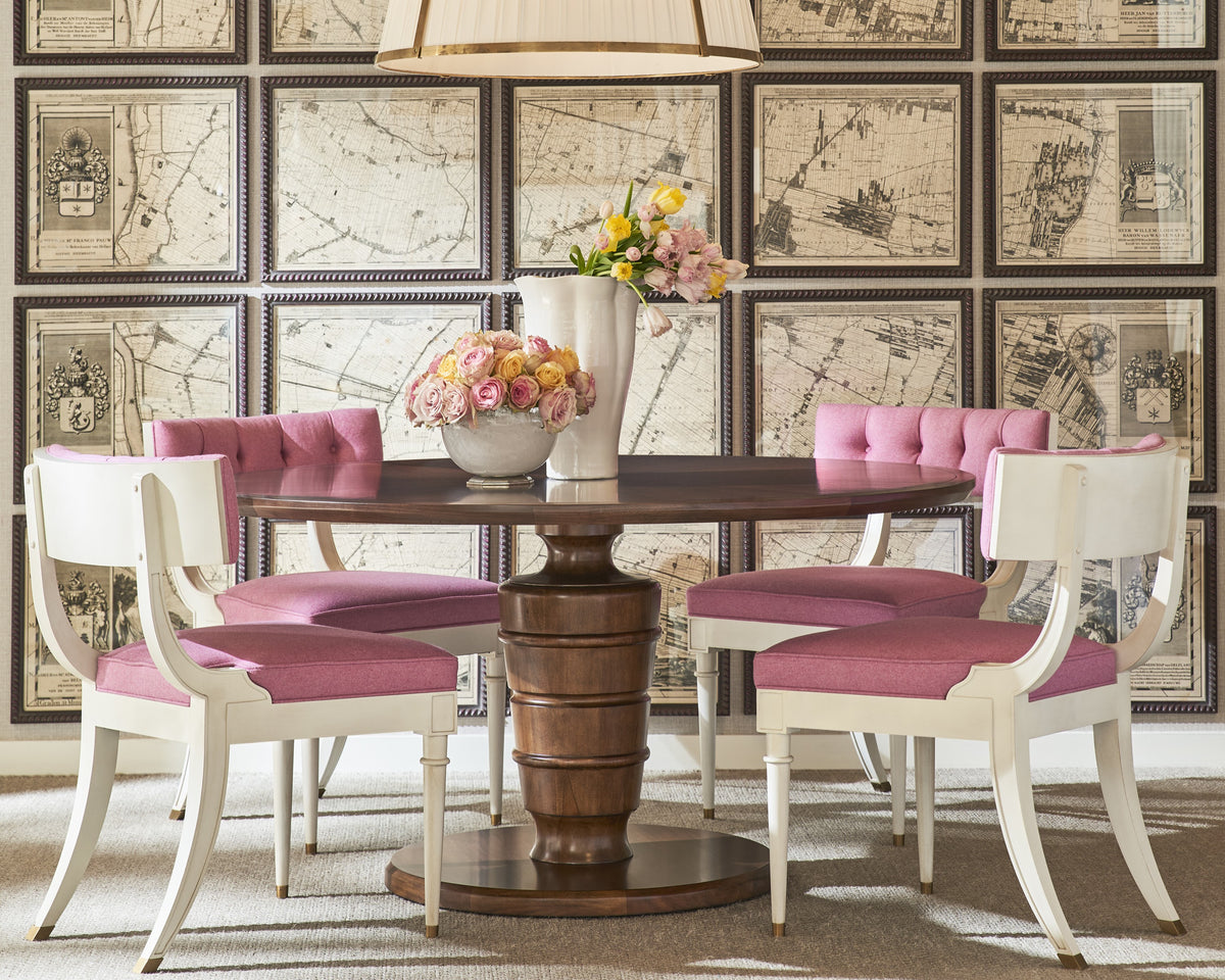 Four pink upholstered dining chairs around a round table with framed maps at Kennedy Galleries Toronto.