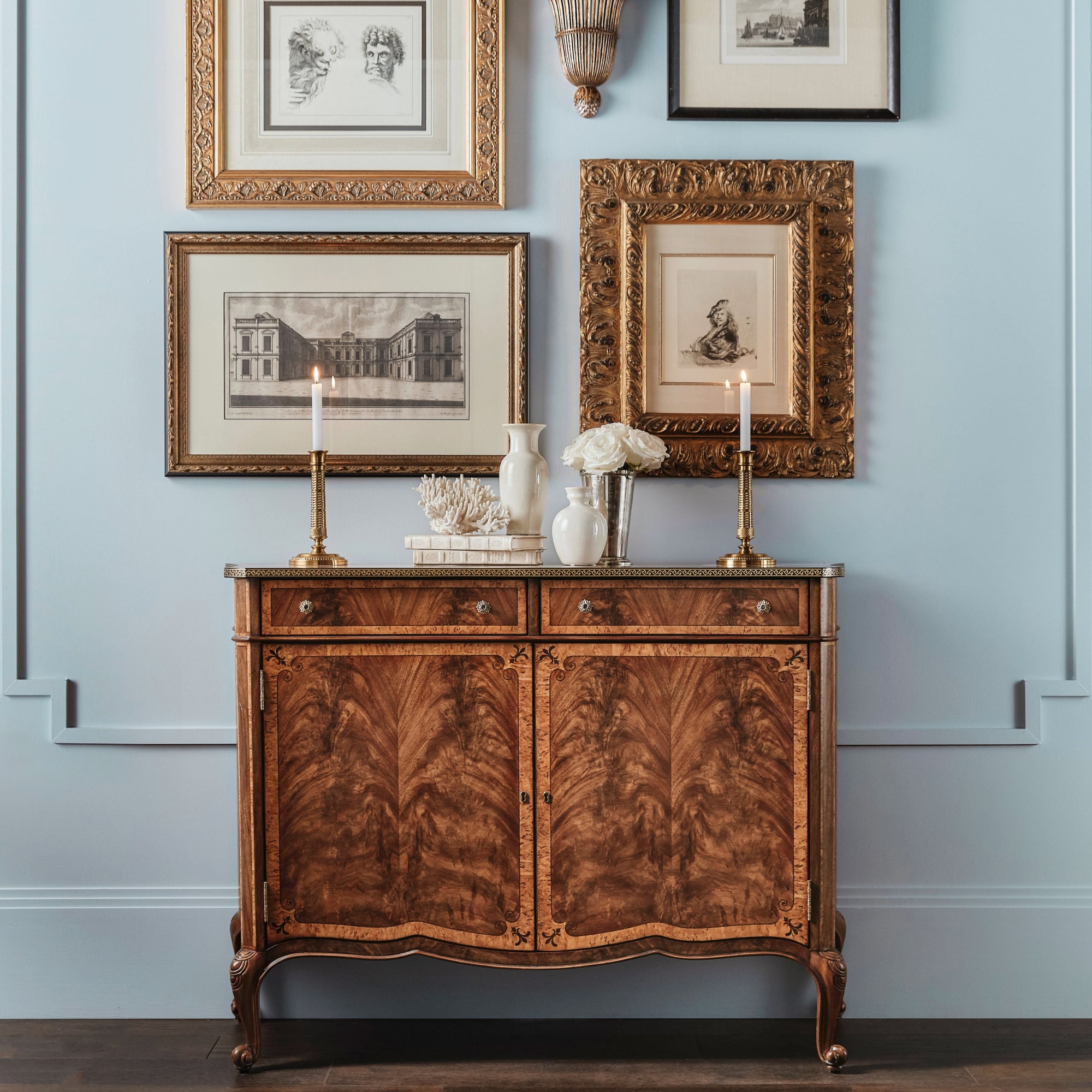 a high quality inlaid mahogany cabinet sits against a light gallery wall filled with hanging art